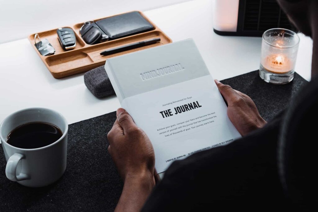 Person holding a journal at a tidy desk with a cup of coffee, a candle, and a wooden tray with small personal items.