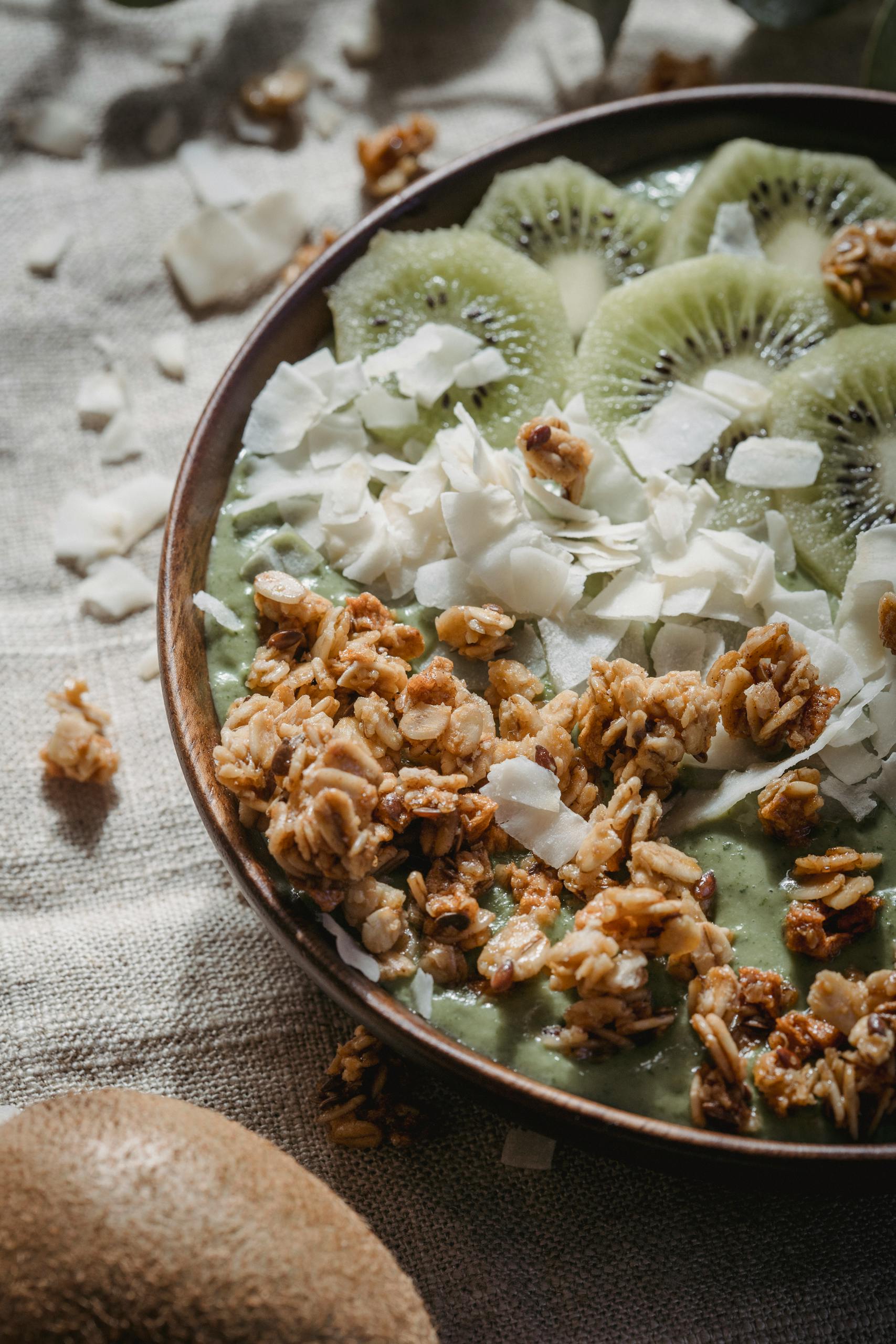 Close-up of a green smoothie bowl topped with kiwi slices, granola, and coconut flakes.