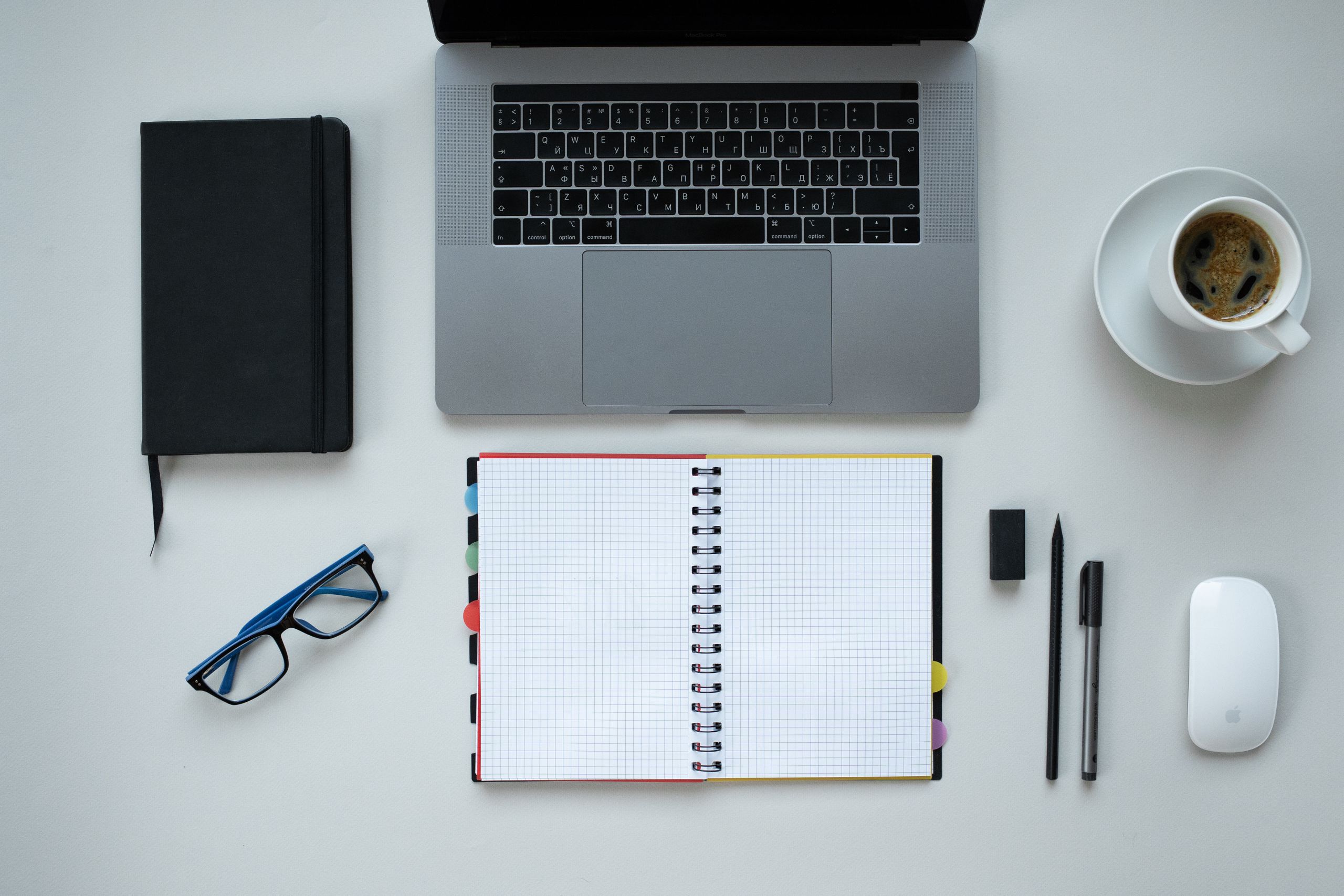 Overhead view of a desk with a laptop, notebook, coffee, and office supplies.