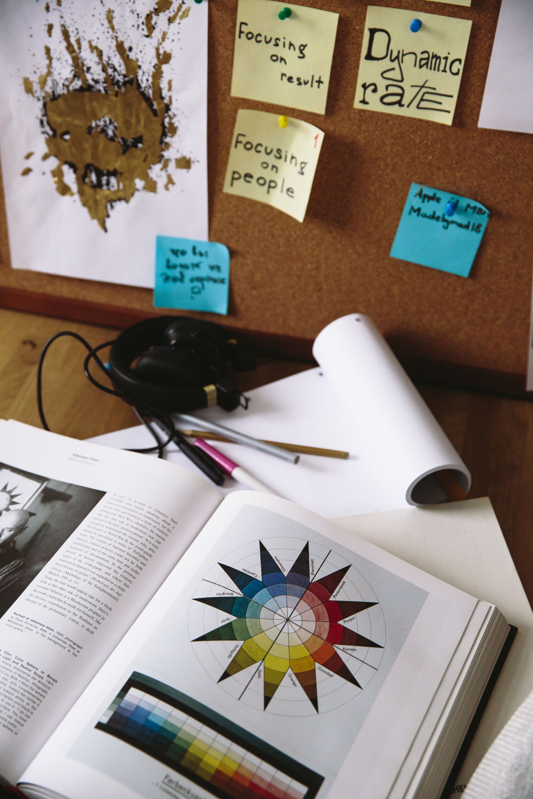 Desk with a color theory book, handwritten idea notes, pens, and design materials.