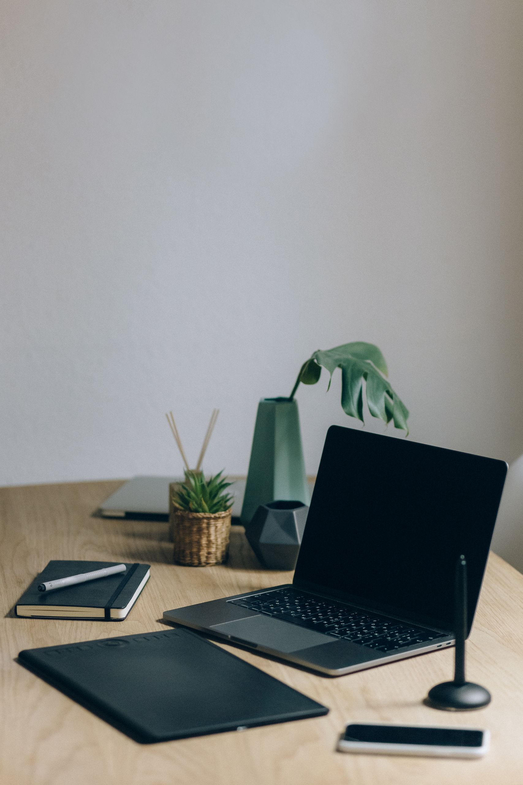 Minimalist home office setup with a laptop, notebook, and plant on a desk.