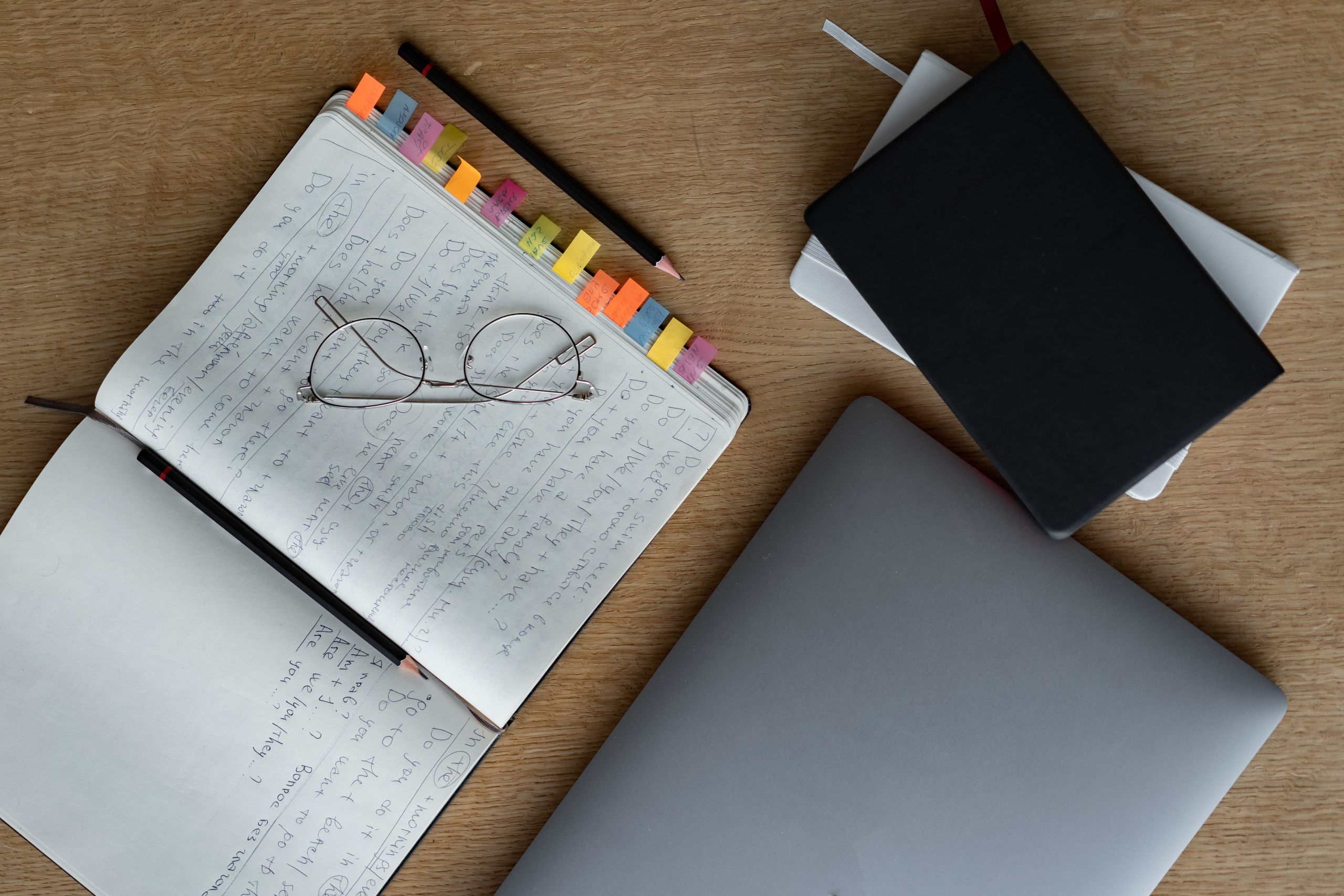 Flat lay of an organized desk with notebooks, eyeglasses, and a laptop, ideal for studying or office work.