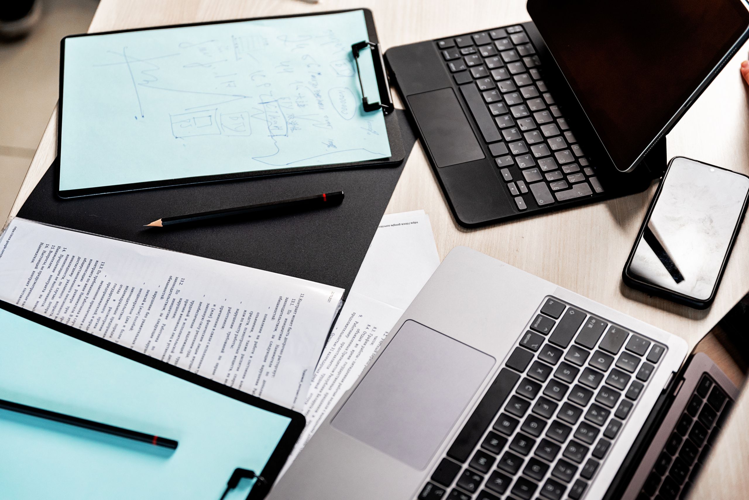 High-angle view of a modern workspace with laptops, a tablet, clipboard, and documents.