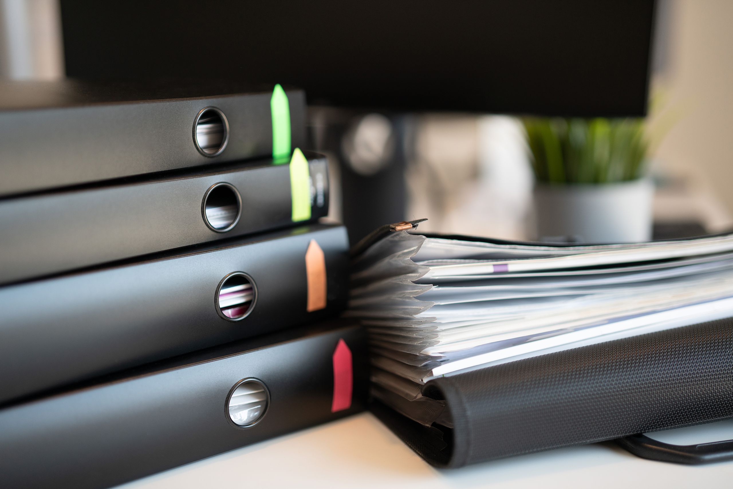 Stack of colorful ring binders and documents on a modern office desk.